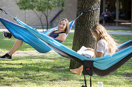 Two female students reading in hammocks and smiling